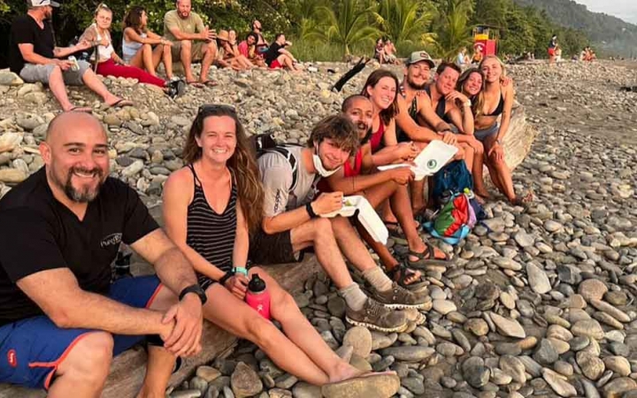 a group of gap year students sit on a rocky beach on an outward bound expedition